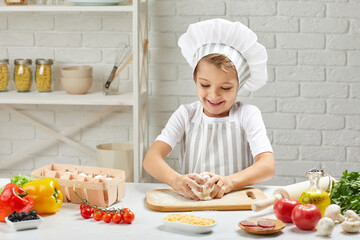 little child boy in cap and an apron playing with dough in the kitchen