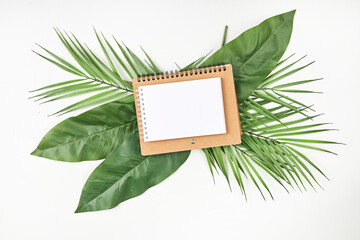 White blank note paper and big green tropical leaves on background. Flat lay. Top view. Copy space.