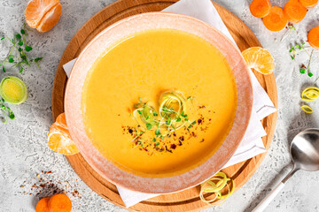 Tasty carrot creamy soup with herbs and spices in a bowl on a grey background top view.  Autumn or winter food. Pureed vegetable soup.