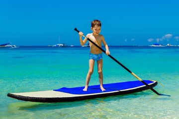Obraz premium Happy little boy have fun on a paddleboard in the tropical sea. The concept of travel and family holidays.
