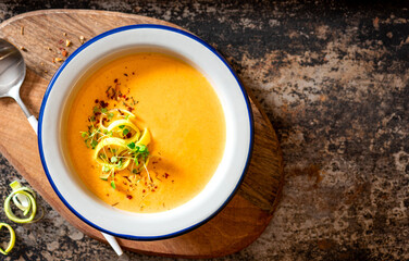 Tasty carrot creamy soup with herbs and spices in a bowl on a dark background top view. Copy space for text. Autumn or winter food. Pureed vegetable soup.