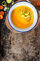 Tasty carrot creamy soup with herbs and spices in a bowl on a dark background top view. Copy space for text. Autumn or winter food. Pureed vegetable soup.