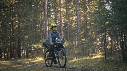 Fototapeta na wymiar The woman travel on mixed terrain cycle touring with bike bikepacking. The traveler journey with bicycle bags. Magic forest park.