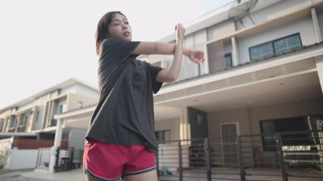 Asian woman doing shoulder arms stretching before exercise ,muscle injury prevention, heating up body before running, human metabolism and immune system, outside neighborhood street exercising routine