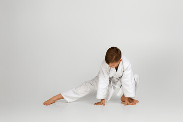 little child boy in a white karate kimono over gray background