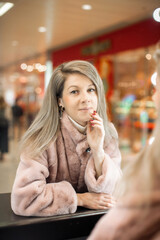 A girl in a beige fur coat among the lights of the shopping center