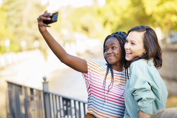 Two multiethnic female friends making selfie outdoors.