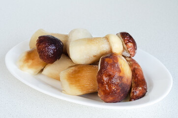 Frozen whole mushrooms are thawed on a white plate. Soft selective focus