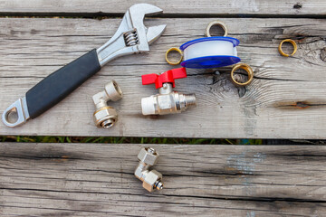 Various plumbing spare parts, sealing tape and adjustable wrench on rustic wooden background. Top view