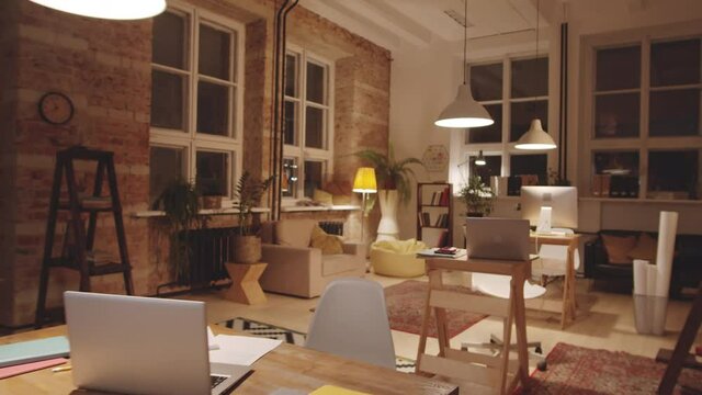 Zoom out dolly shot of modern open space office with loft interior and comfortable workplaces. No people are inside