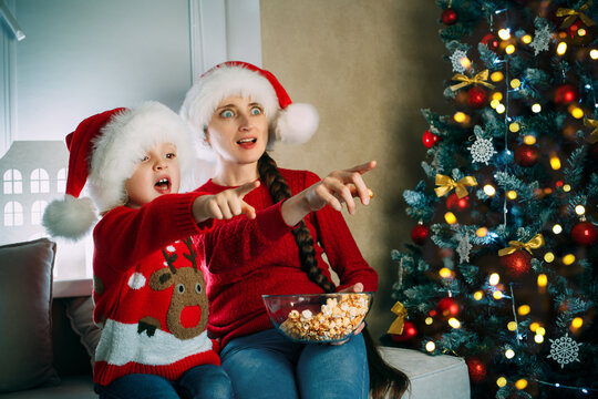 A young mother and her daughter watch movies at home on Christmas day pointing at the screen
