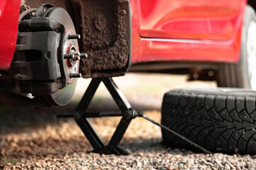 The front hub of a red car without a wheel. A raised car with the wheel removed. The concept of puncturing a tire or replacing a summer wheel with a winter one with your own hands