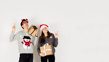 Young couple in Christmas sweaters pointing up on white background