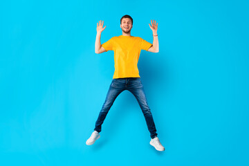 Happy guy jumping over blue studio wall
