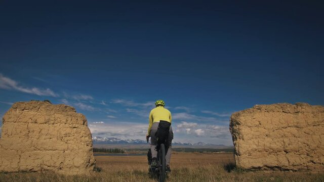 The man travel on mixed terrain cycle touring with bikepacking. The traveler journey with bicycle bags. Sport bikepacking, bike, sportswear in green black colors. Mountain snow capped, stone arch.
