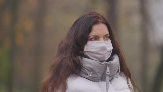 Pretty pregnant woman in face mask walks on footpath in autumn park. Brunette woman with long hair in Catherine Park, Tsarskoye Selo, Saint Petersburg, Russia.