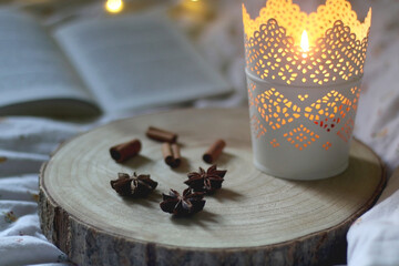 Wooden tray with anise and cinnamon, lit candle and open book. Selective focus, bokeh lights.