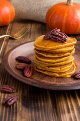 Homemade pumpkin pancakes with honey and pecans in the ceramic plate on the rustic background