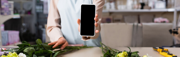 Cropped view of florist showing smartphone with blank screen near desk with eustoma flowers on blurred background, banner