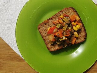  black bread toast with slices of pepper, tomato, herbs and zucchini on a green plate