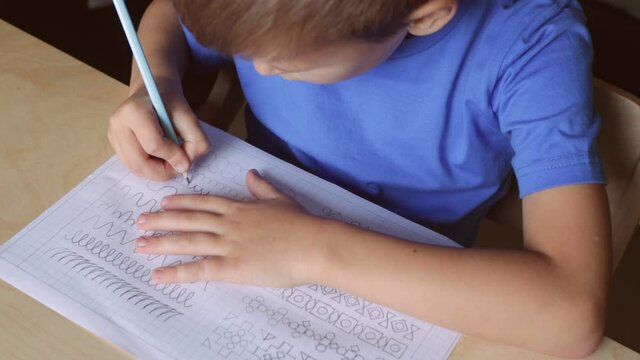 Cute kid tracing lines on paper with pencil. Doing home lesson. Children education concept.
