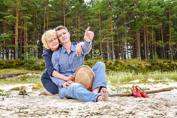 happy man and woman sitting on the sand near the sea