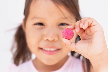 A little girl holding up a sugar candy vitamin. Children supplements.