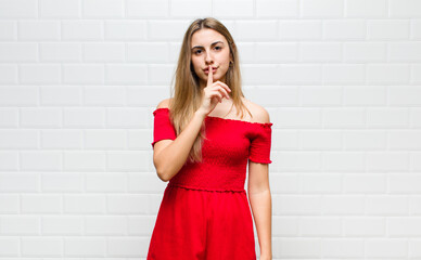 blonde woman looking serious and cross with finger pressed to lips demanding silence or quiet,...