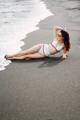 Brunette girl laying on the hidden black sand beach wearing a cute bathingsuit in Bali Indonesia