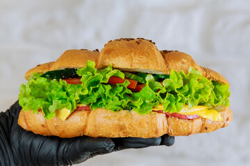 Fresh croissant with ham and salad in the hand of a waiter in a black glove