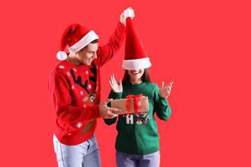 Man presenting Christmas gift to his girlfriend on red background