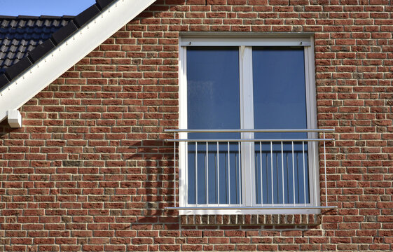 Fassade eines modernen neu gebauten Fertighauses mit Vorsatz-Verklinkerung und Fallschutzgeländer aus Edelstahl vor dem Fenster