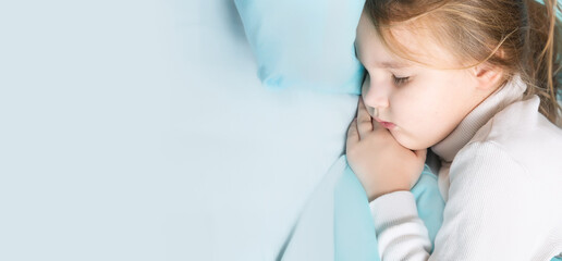 Little brunette girl sleeps sweetly in bed with blue linen. space for text. healthy baby's sleep. top view