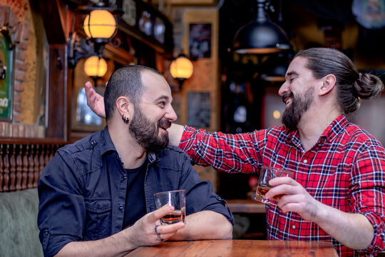 Two cheerful male friends embracing and laughing, drinking whiskey together at the pub. Celebrating life.