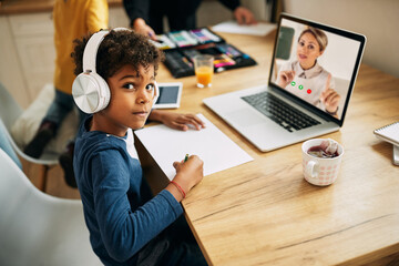 African American boy with headphones following online class over laptop from home.
