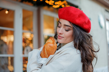 Portrait of a young beautiful woman in a red beret in a European city. Young woman holds a paper bag with baguettes. Christmas.
