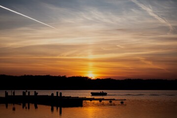 Piękny zachód słońca nad największym jeziorem w Polsce i płynącą łódką. - obrazy, fototapety, plakaty