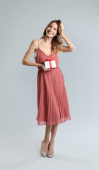 Naklejka premium Beautiful young woman with Christmas present on light grey background
