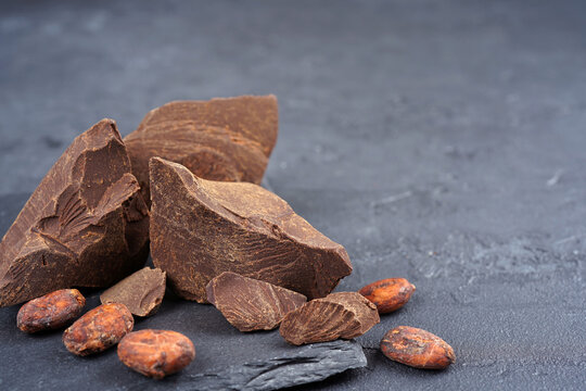 Cocoa liquor mass, beans on slate stand, gray concrete background. Confectionery, menu, recipe concept. Close-up, copy space