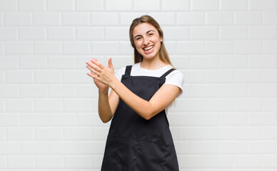 blonde woman feeling happy and successful, smiling and clapping hands, saying congratulations with...