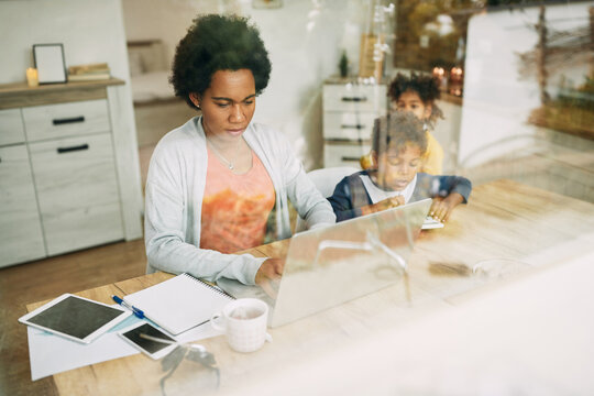 African American Single Mother With Two Kids Working On Laptop At Home.