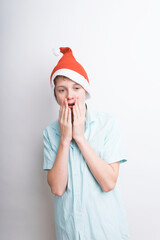 Cute Caucasian teenage boy in Santa Claus hat is surprised by something. Isolated on a white background