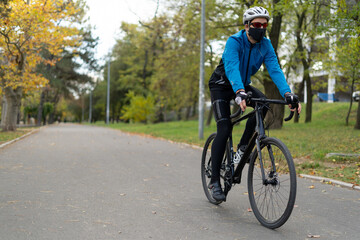 A young man in a protective mask and helmet rides a bicycle on the road. Active rest in quarantine. Fighting excess weight.