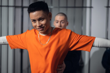 An armed guard searches a newly arrived criminal in a prison corridor against a backdrop of bars