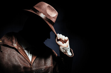 Fototapeta premium Photo of a shaded detective portrait in jacket putting on hat on black background.