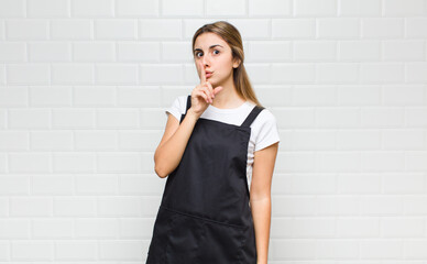 blonde woman asking for silence and quiet, gesturing with finger in front of mouth, saying shh or...