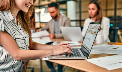 Glad to be on the team. Beautiful cheerful woman working at a laptop sitting at an office table with her colleagues.