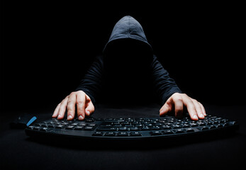 Photo of a shaded evil hacker theaf in black hoodie typing on keyboard.