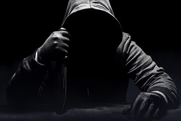 Scary horror photo of a man  in black hoodie sitting with knife.