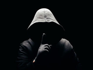 Photo of a scary horror man in hoodie showing silence hand sign in dark. - obrazy, fototapety, plakaty